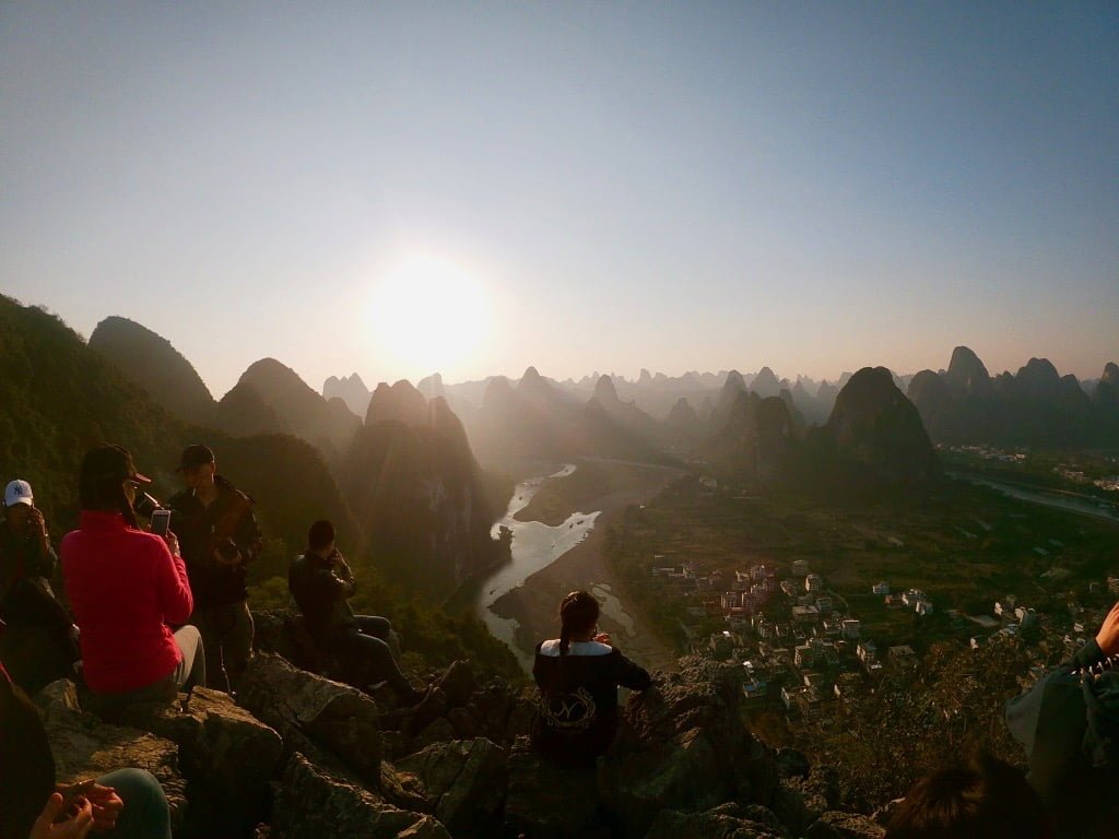 People sitting on rocks admiring the mountain view from Laozhai Hill in Xingping