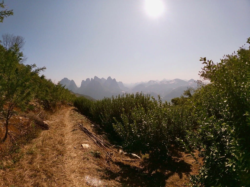 A dirt path, a blazing sun, and shadowy karst mountains while hiking near Guilin