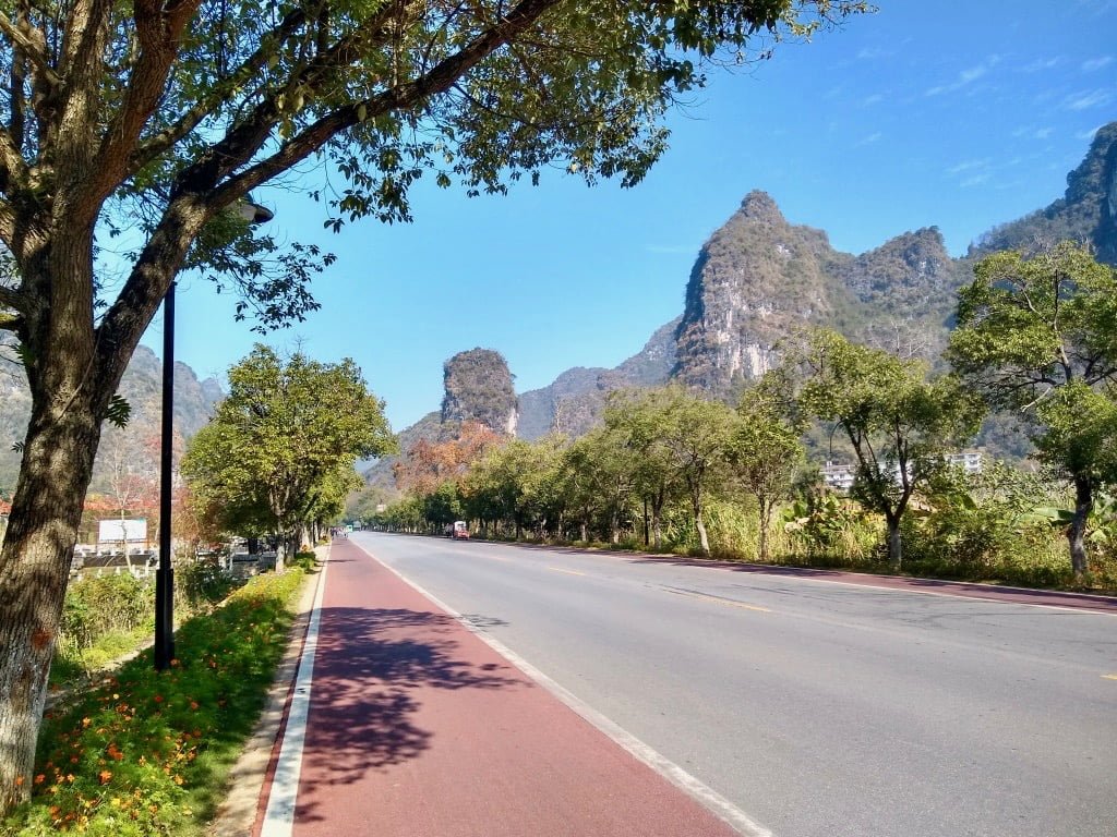 The 10-Mile Gallery Path in Yangshuo, featuring a red bike lane, a driving road, and beautiful scenery of the karst mountains