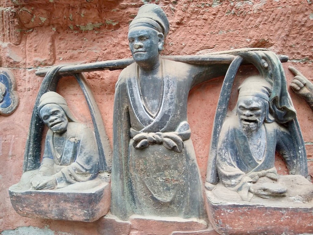 A statue depicting Confucius belief in filial piety; the man is seen carrying his two parents. Location: Dazu Rock Carvings, baodingshan site, Chongqing, China