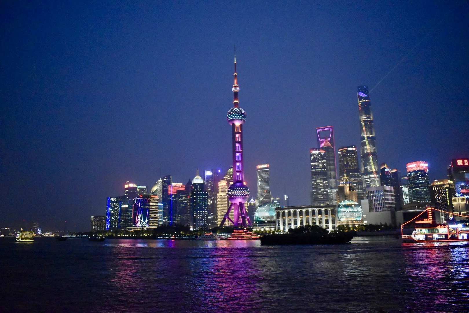 Forced to wrong size: 923x615, natural is 1620x1080! A night-time skyline view of Shanghai, China buildings, including a thin building with a circular portion that is the TV tower.