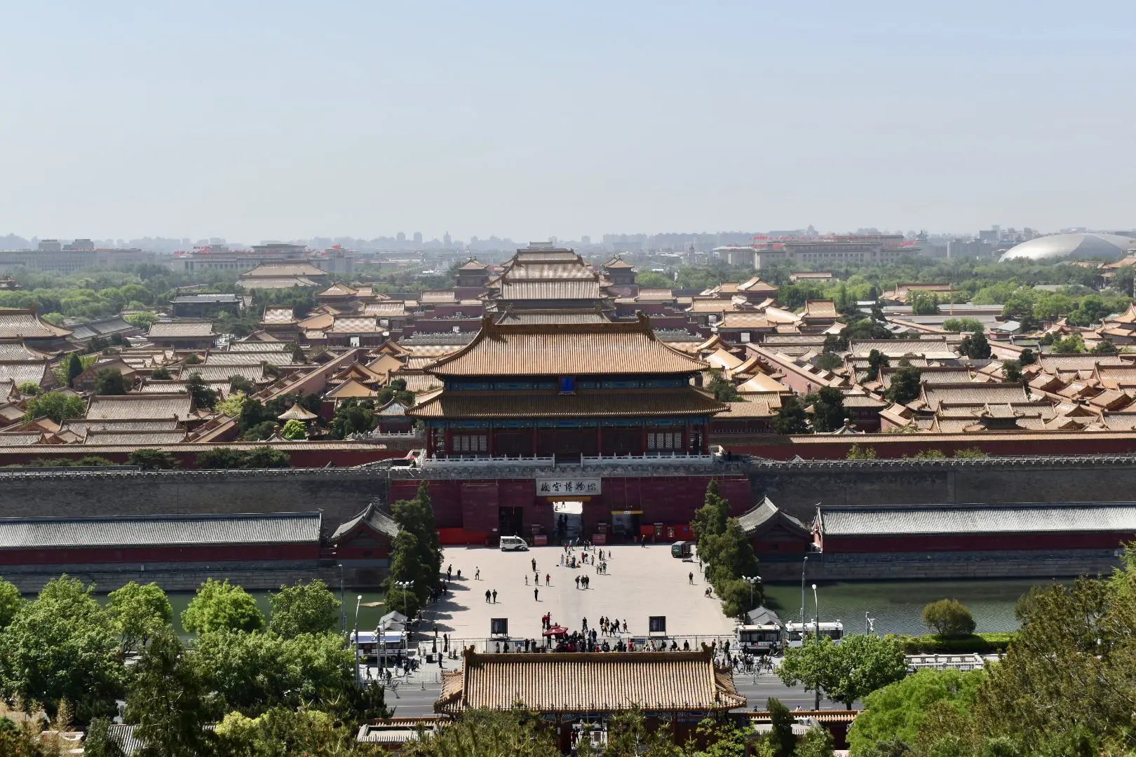 Forced to wrong size: 923x615, natural is 1620x1080! A large gold-roofed building with a grey wall and many smaller gold-roofed buildings behind it. Green trees in front. Location: Forbidden City, Beijing, China as seen from Jingshan Park.